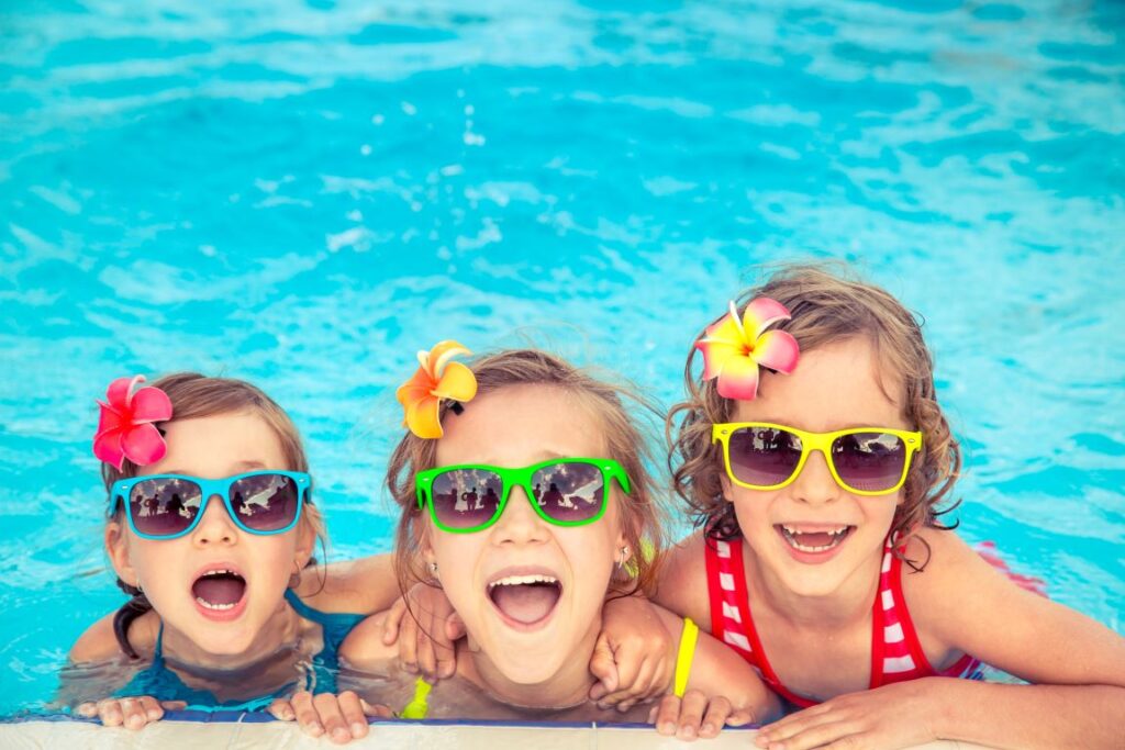 Three little girls wearing sunglasses and swimming in a swimming pool.